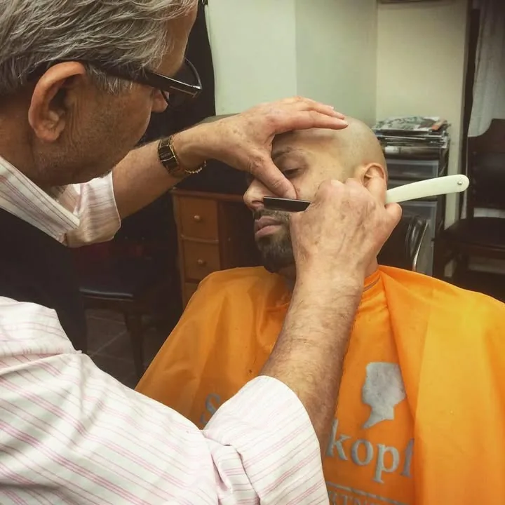 Barbier réalisant une taille de barbe au rasoir droit